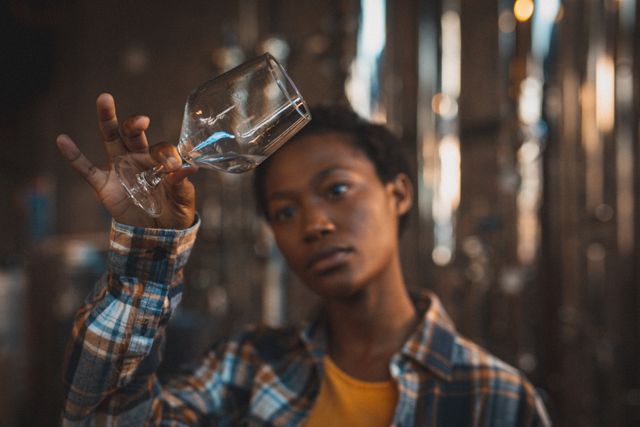 African american woman working at gin distillery, holding up a glass and inspecting product - Download Free Stock Photos Pikwizard.com