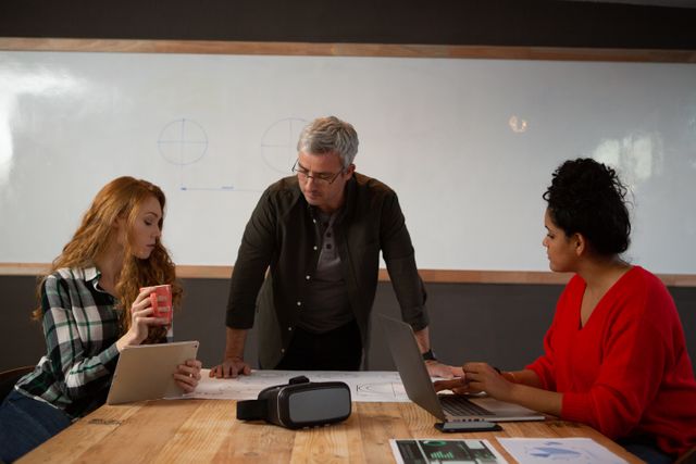 Front view of a Caucasian man, a Caucasian woman and a mixed race woman working in a creative office, brainstorming in a conference room, with a whiteboard in the background
