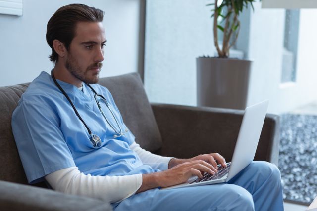 Male surgeon using laptop on sofa in lobby at hospital - Download Free Stock Photos Pikwizard.com