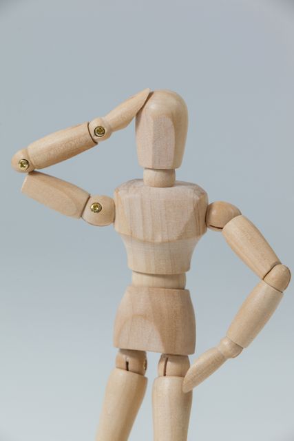 Confused wooden figurine standing with hand on head against grey background
