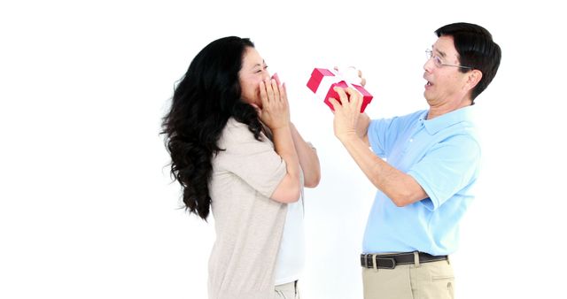 A middle-aged Asian man joyfully surprises a woman with a gift, hinting at a celebration. - Download Free Stock Photos Pikwizard.com