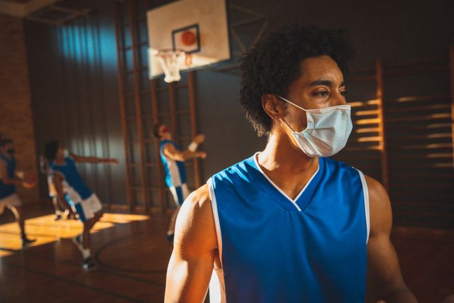 Mixed race male basketball player wearing face mask, practicing with team in sunlit indoor court - Download Free Stock Photos Pikwizard.com