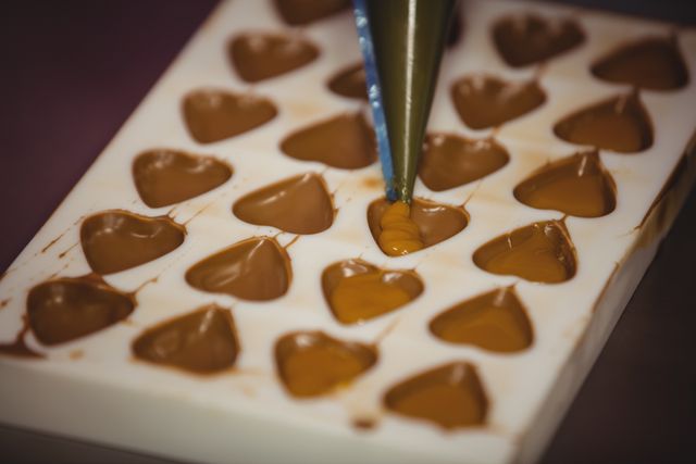 Filling a chocolate mould with a piping bag in factory