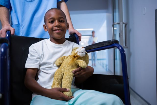 Portrait of boy sitting on wheelchair and holding teddy bear in corridor - Download Free Stock Photos Pikwizard.com