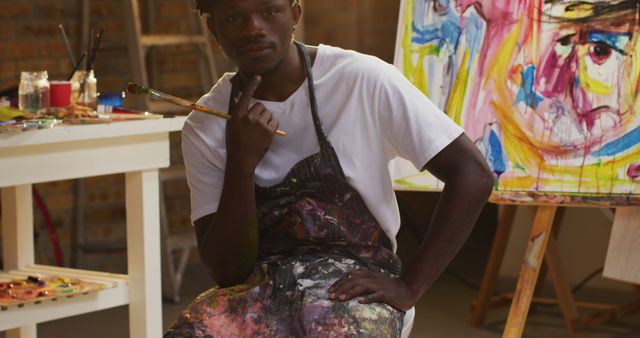 Portrait of african american male artist wearing apron holding a paint brush smiling at art studio - Download Free Stock Photos Pikwizard.com