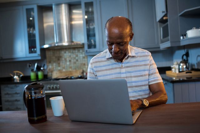 Senior man using laptop at table in kitchen - Download Free Stock Photos Pikwizard.com