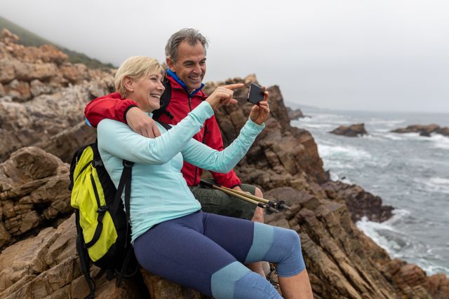 Caucasian hiker senior couple using smartphone while sitting on the rocks - Download Free Stock Photos Pikwizard.com