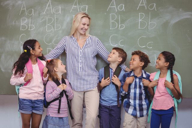 Happy teacher standing with schoolkids in classroom - Download Free Stock Photos Pikwizard.com
