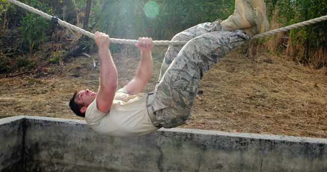 A military man trains outdoors, climbing a rope with intense focus