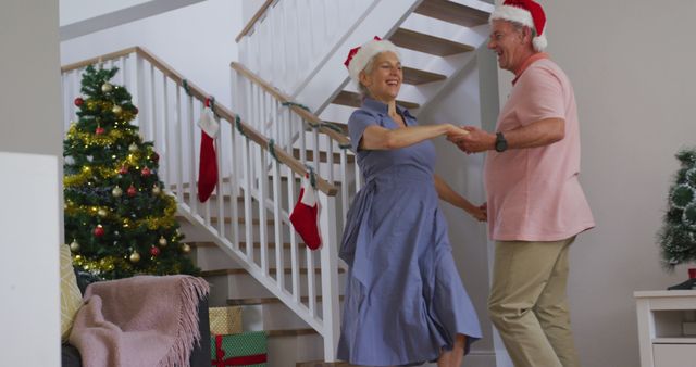 Happy caucasian senior couple wearing santa hats and dancing at christmas time. christmas, festivity and tradition at home.