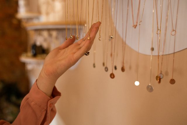 Hand of caucasian female customer touching necklaces hanging on display in jewellery shop - Download Free Stock Photos Pikwizard.com