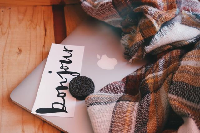 close up view of bonjour text on a placard, Oreo biscuit and blanket over a laptop. cozy winter concept