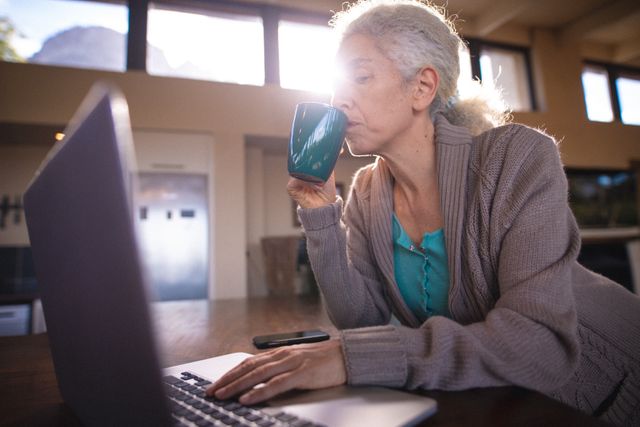 Caucasian senior woman drinking coffe and using laptop. retirement lifestyle, spending time alone at home.