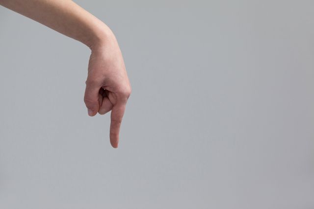 Hand of a woman pointing downwards against grey background