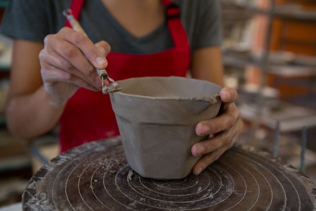 Mid section of female potter molding a mug with hand tool