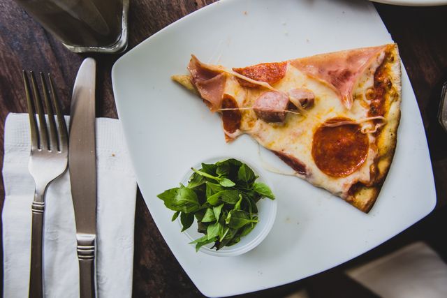 Close up of pizza slice in a dish and cutlery on wooden table at restaurant. food and restaurant concept