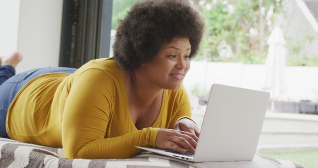Image of happy plus size african american woman lying on floor and using laptop. lifestyle, leisure, spending free time at home with technology.