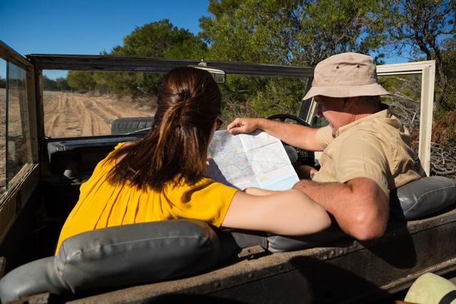 Couple reading map while sitting in off road vehicle on sunny day