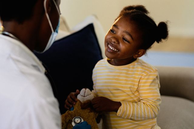 Smiling african american girl having medical visit with doctor wearing face mask - Download Free Stock Photos Pikwizard.com