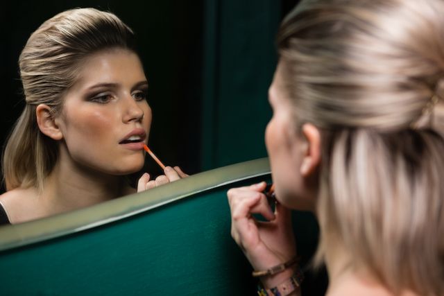 Woman applying lips gloss while looking at mirror - Download Free Stock Photos Pikwizard.com