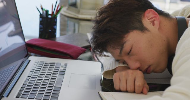 Asian male teenager with headphones sleeping and using laptop in living room - Download Free Stock Photos Pikwizard.com