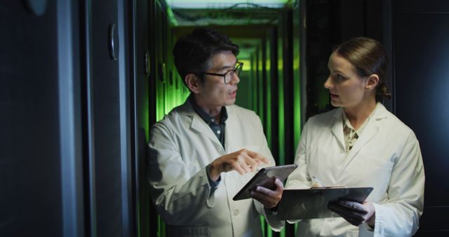 Diverse female and male it technicians in lab coats using tablet and laptop checking computer server. information technology, data processing and computer servers.
