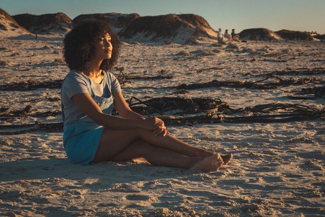 African american woman sitting on beach and relaxing during sunset - Download Free Stock Photos Pikwizard.com