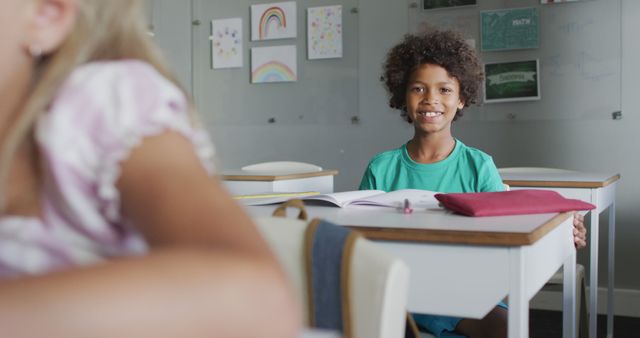 Image of happy biracial boy sitting at desk in classsroom. primary school education and learning concept.