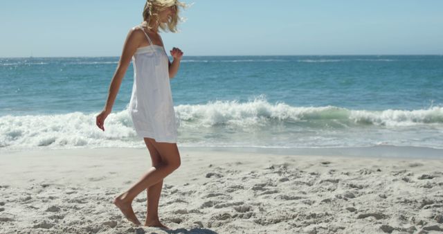 Happy caucasian woman wearing white dress and walking at beach on sunny day. Vacation, free time and relax.