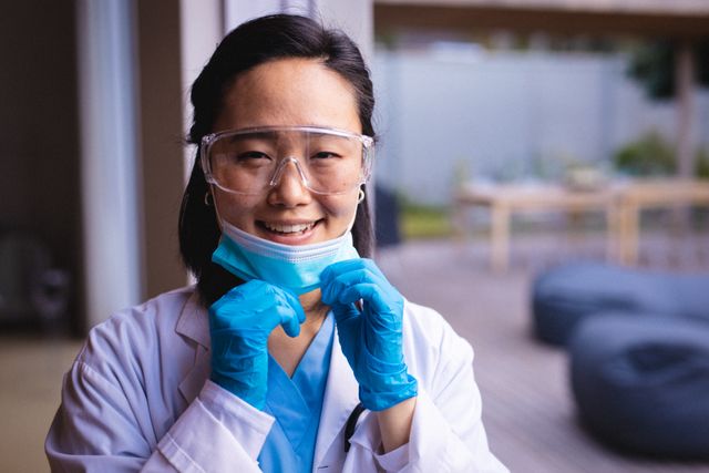 Portrait of smiling asian doctor wearing protective glasses and face mask looking at camera - Download Free Stock Photos Pikwizard.com