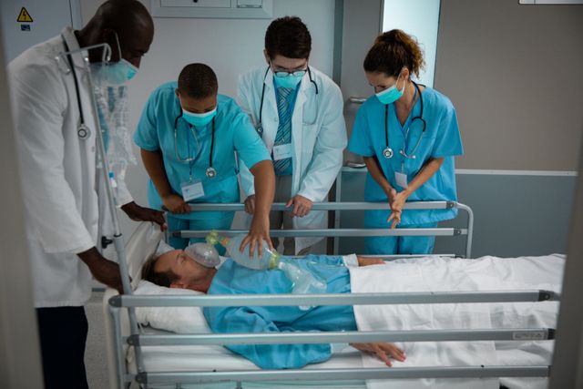 Diverse group of male and female doctors wearing face masks pushing patient in bed through corridor - Download Free Stock Photos Pikwizard.com
