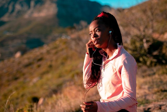 Fit african american woman resting between exercise in countryside, wearing wireless earphones. healthy active lifestyle and outdoor fitness.