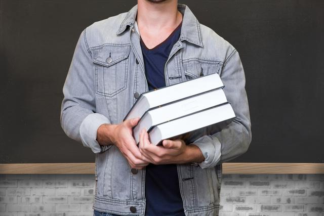 Midsection of student holding books against blackboard - Download Free Stock Photos Pikwizard.com