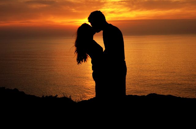 Silhouette of a couple kissing against sunset sky over sea. couple, love and relationship concept
