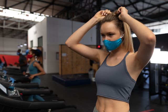Caucasian woman wearing a blue mask inside the gym fixing her hair - Download Free Stock Photos Pikwizard.com