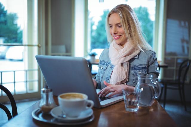Smiling woman using laptop while having coffee - Download Free Stock Photos Pikwizard.com
