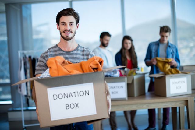 Smiling man holding a donation box in office - Download Free Stock Photos Pikwizard.com