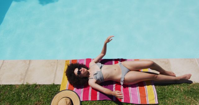 Mixed race woman lying on blanket sunbathing by the pool from