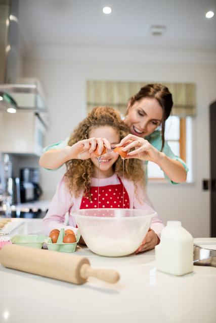 Mother assisting daughter in breaking eggs in kitchen - Download Free Stock Photos Pikwizard.com