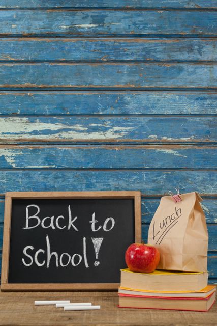 Apple, lunch bag, books and slate with back to school text against blue wooden background
