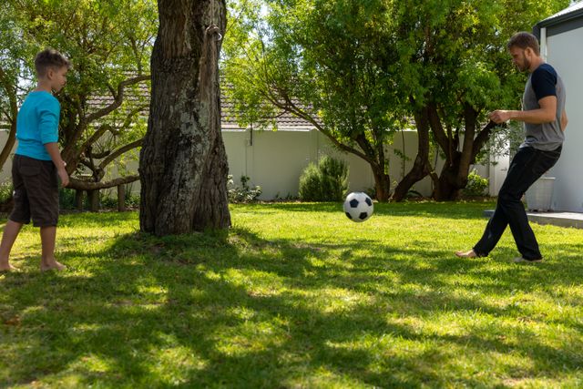 Caucasian dad and his son playing football in their backyard during a bright and sunny day - Download Free Stock Photos Pikwizard.com