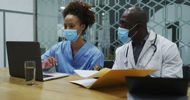 Diverse female and male doctors wearing face masks using laptop and talking in office. medical professional working in health centre hospital office during covid 19 coronavirus pandemic.