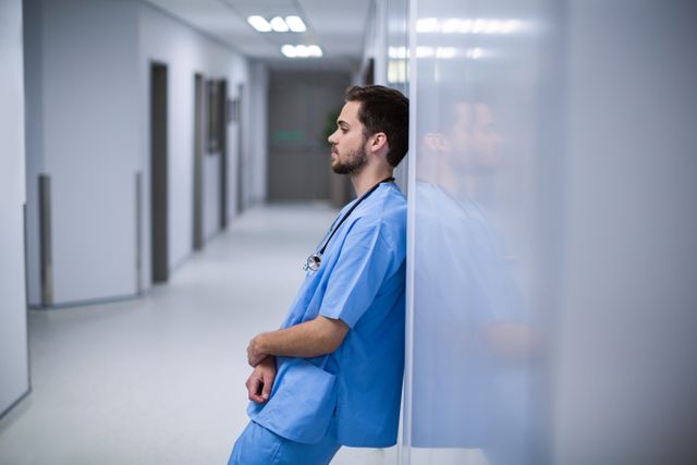 Tensed male nurse leaning on wall in corridor - Download Free Stock Photos Pikwizard.com