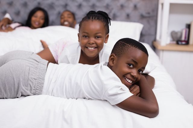 Portrait of smiling siblings lying with parents in background on bed at home