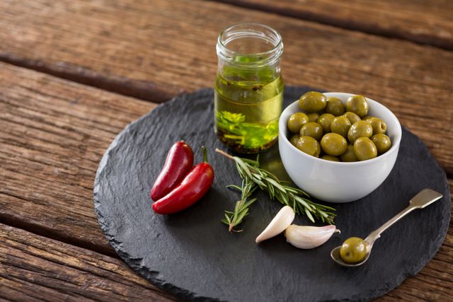 Close-up of green olives, fresh herbs with olive oil and red chilies on table