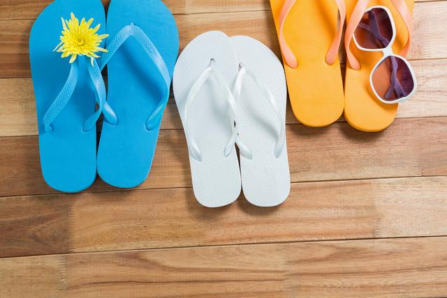 Three pairs of beach flip flop slippers and sunglasses on wooden board