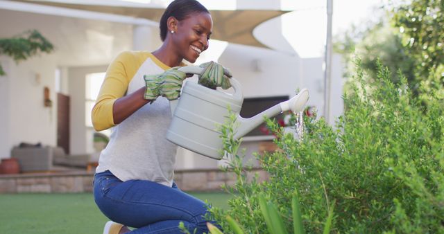 Happy african amercian woman gardening, watering plants in garden. staying at home in self isolation during quarantine lockdown.