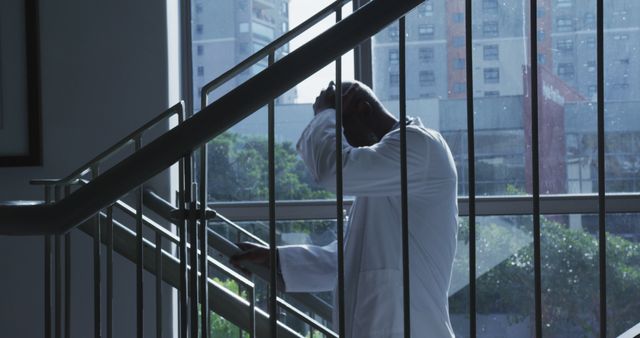 Tired african american male doctor standing on the staircase in hospital. medicine, health and healthcare services.