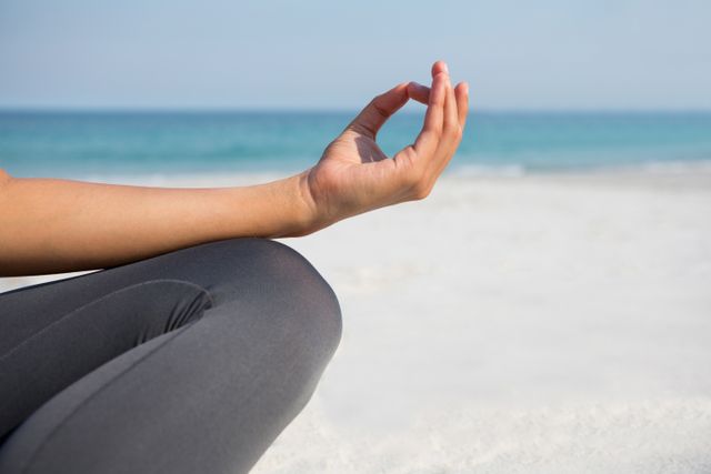 Cropped image of woman meditating at beach on sunny day