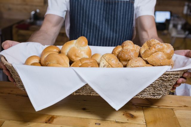 Mid section of waiter holding basket of baked pastries at counter in cafe